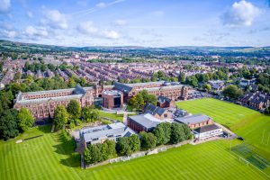 Bolton School's iconic red sandstone buildings, with the large green spaces of the school's grounds in the foreground and Bolton in the background